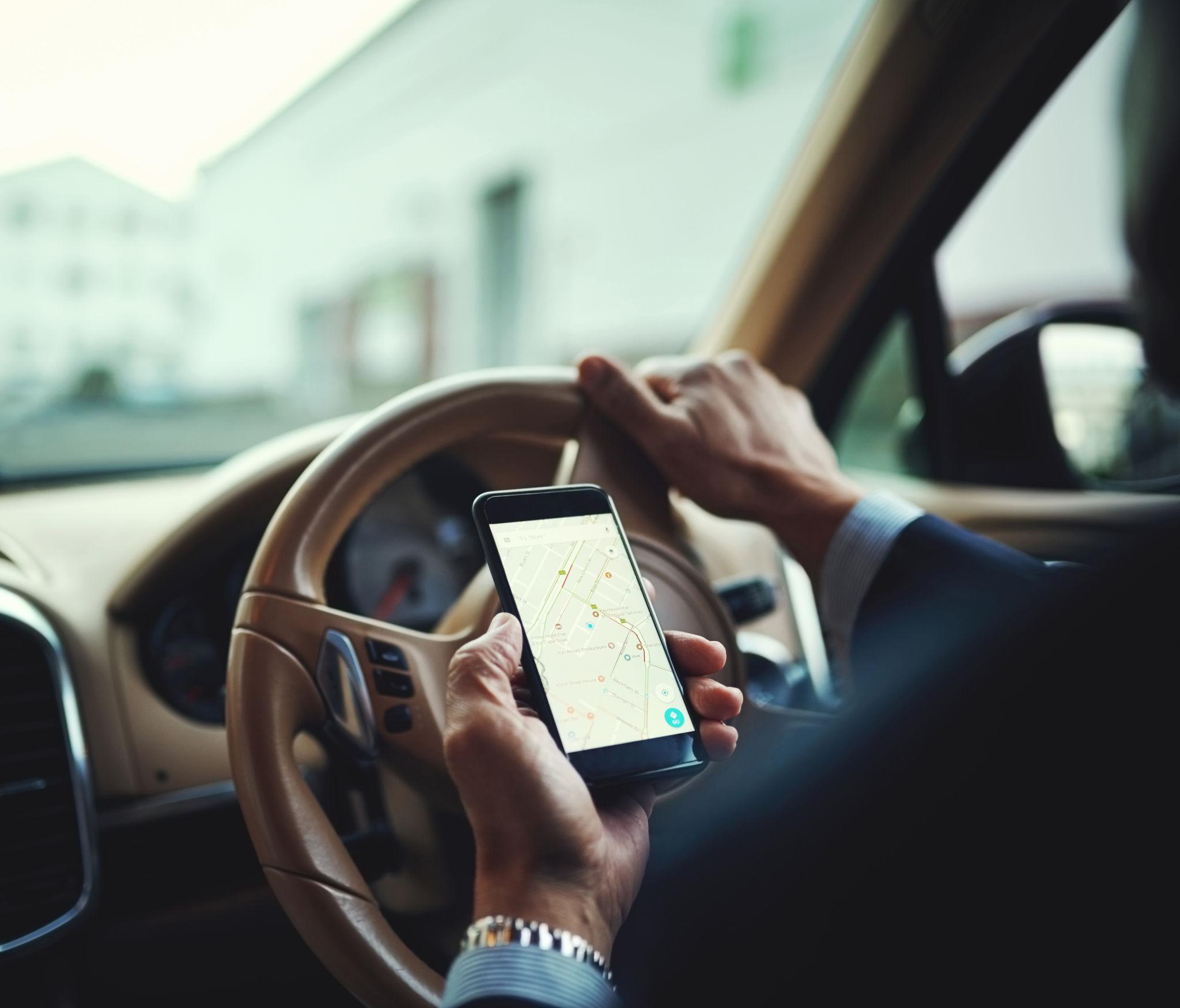 Business owner using a smartphone to track business mileage while sitting in a parked vehicle before a client meeting.
